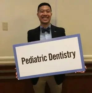 A man holding up a sign that says pediatric dentistry.
